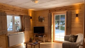 L’intérieur chaleureux d’un chalet avec des murs en bois, une télévision, un canapé et une table.