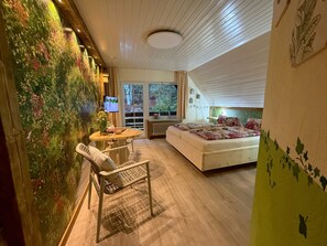 Une chambre à coucher avec un lit, un bureau et une chaise, une télévision et une grande fenêtre.