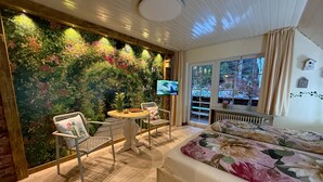 A cozy room with a bed, a table with chairs, a TV, and a large window with a view of greenery.