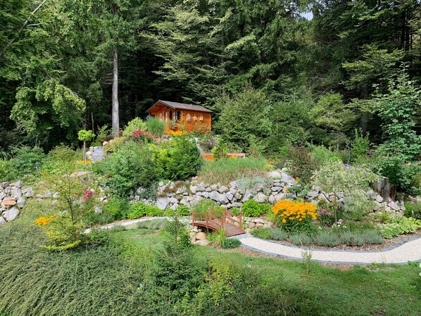 A wooden cabin surrounded by lush greenery and a stone pathway.