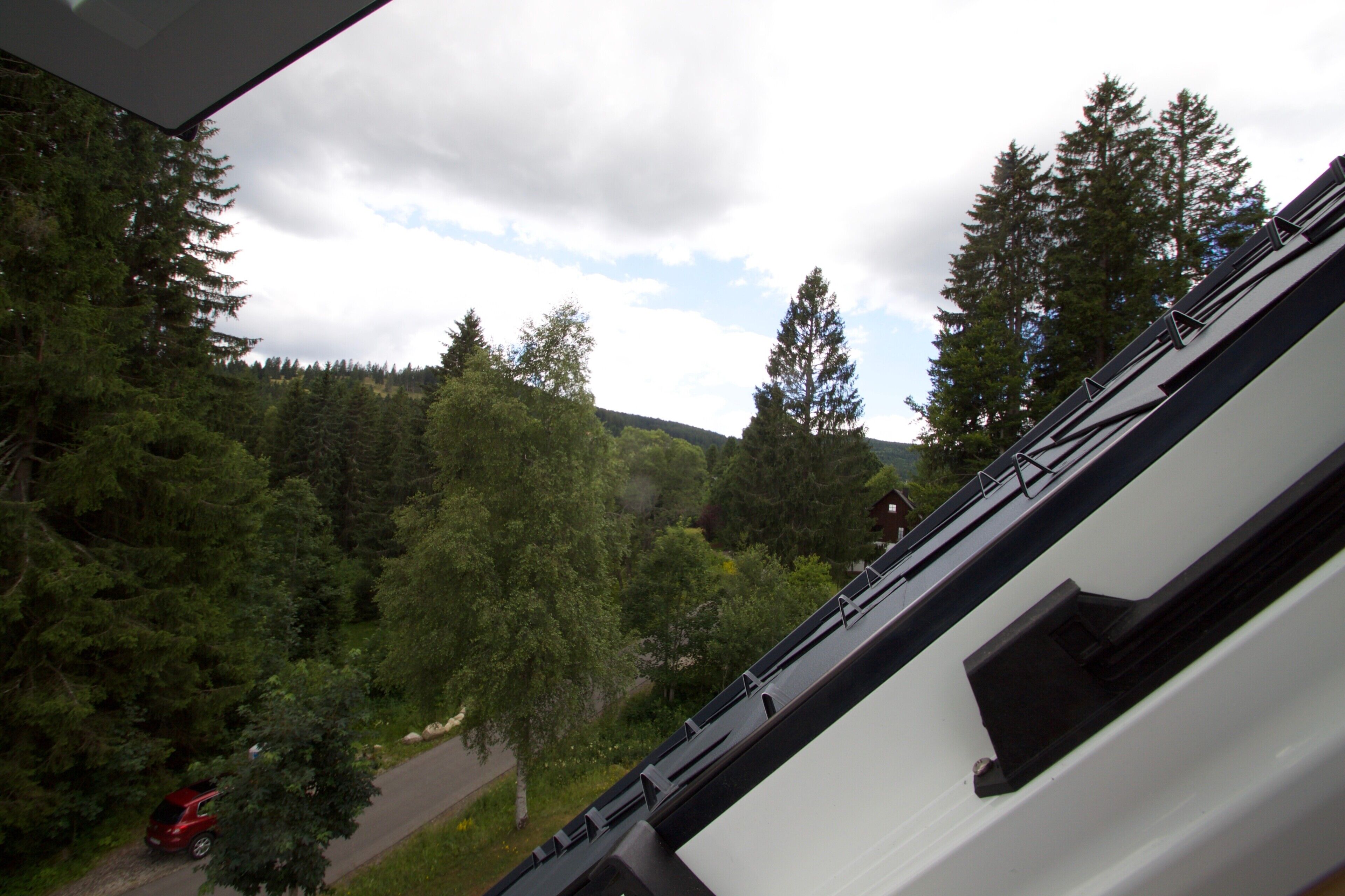 A view from a window overlooking a forested area with a road and a red vehicle.