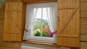 Une pièce en bois avec une fenêtre ornée de rideaux blancs, d’où l’on peut admirer des fleurs.