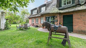 Una casa de ladrillo con techo de paja, una escultura de caballo y un jardín con mesa y sillas.