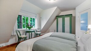 Un dormitorio con una cama, una silla, una mesita, un ventanal y un armario verde.