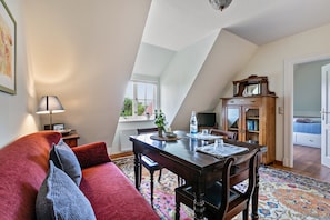 A cozy living room with a red sofa, a dining table, and a wooden cabinet. - Apartment 'Mohnzimmer' with Shared Garden and Wi-Fi (Norddeich)