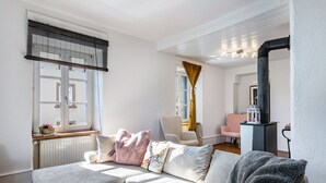 Een woonkamer met een bank, een raam met jaloezieën, een radiator, een stoel en een open haard.