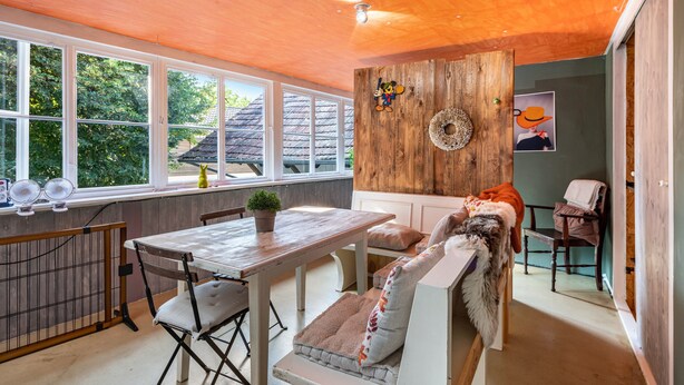 Een gezellige kamer met een houten plafond, een eettafel met stoelen, een bank en uitzicht op het landschap door grote ramen.