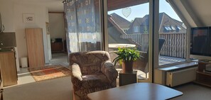 En stue med sofa, sofabord, en potteplante, fjernsyn og udsigt ud af vinduet.