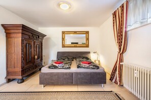 A bedroom with a bed, a wooden wardrobe, a mirror, and a radiator.