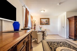 Una habitación con un aparador de madera, un jarrón azul, un cuadro enmarcado, una mesita con un jarrón de flores y una alfombra estampada.