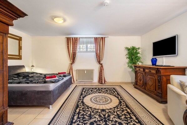 A bedroom with a bed, a dresser, a TV, a radiator, and a window with curtains.
