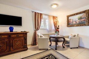 Una sala de estar con un televisor, un mueble de madera, dos sofás blancos, una mesa redonda y una alfombra estampada.