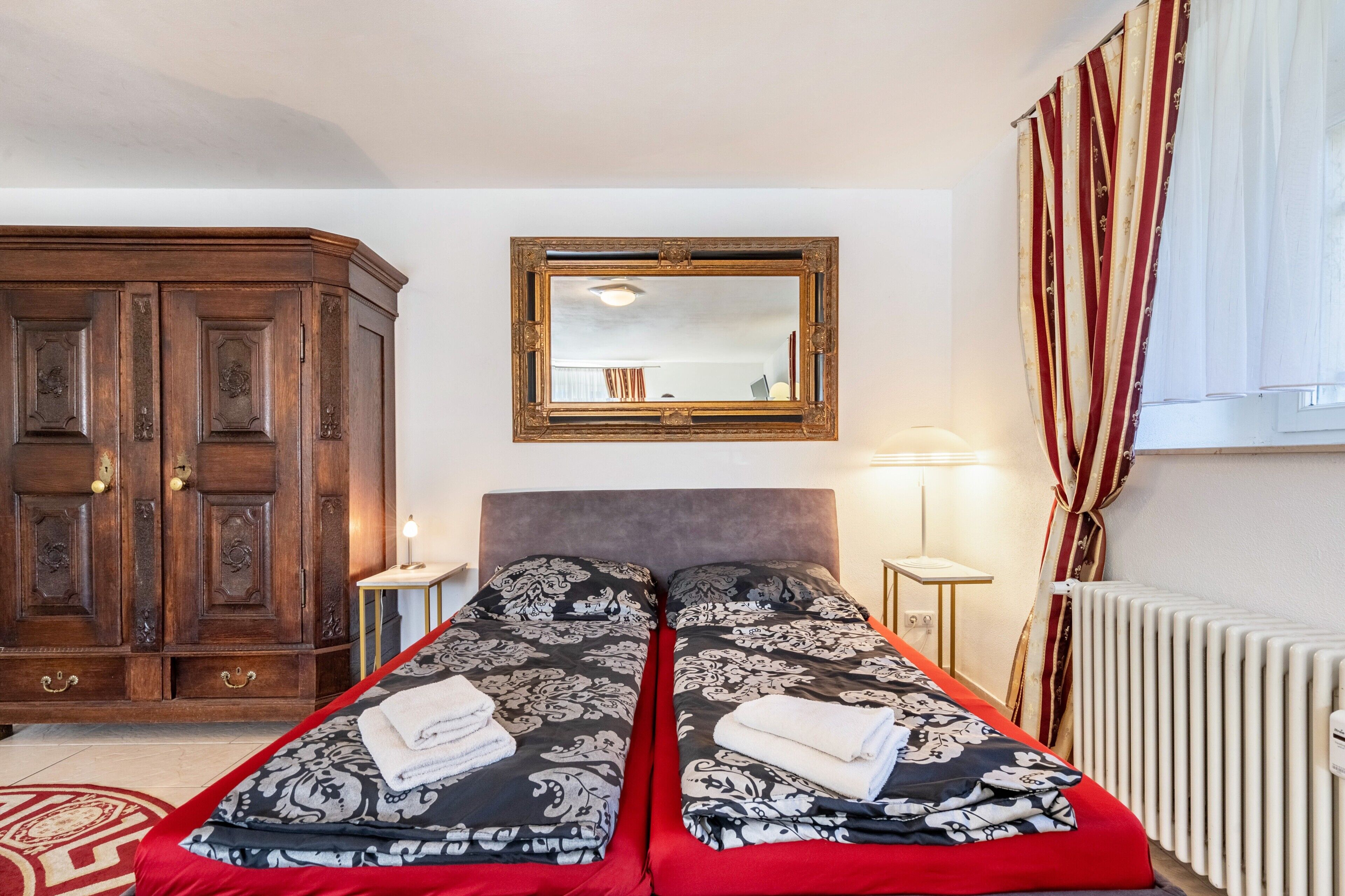 Ein Doppelbett mit gemusterten Betttextilien, ein Holzschrank, ein Spiegel, ein Nachttisch und eine Heizung.