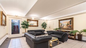 Een ruime woonkamer met twee zwarte leren banken, een glazen salontafel en een groot schilderij aan de muur.