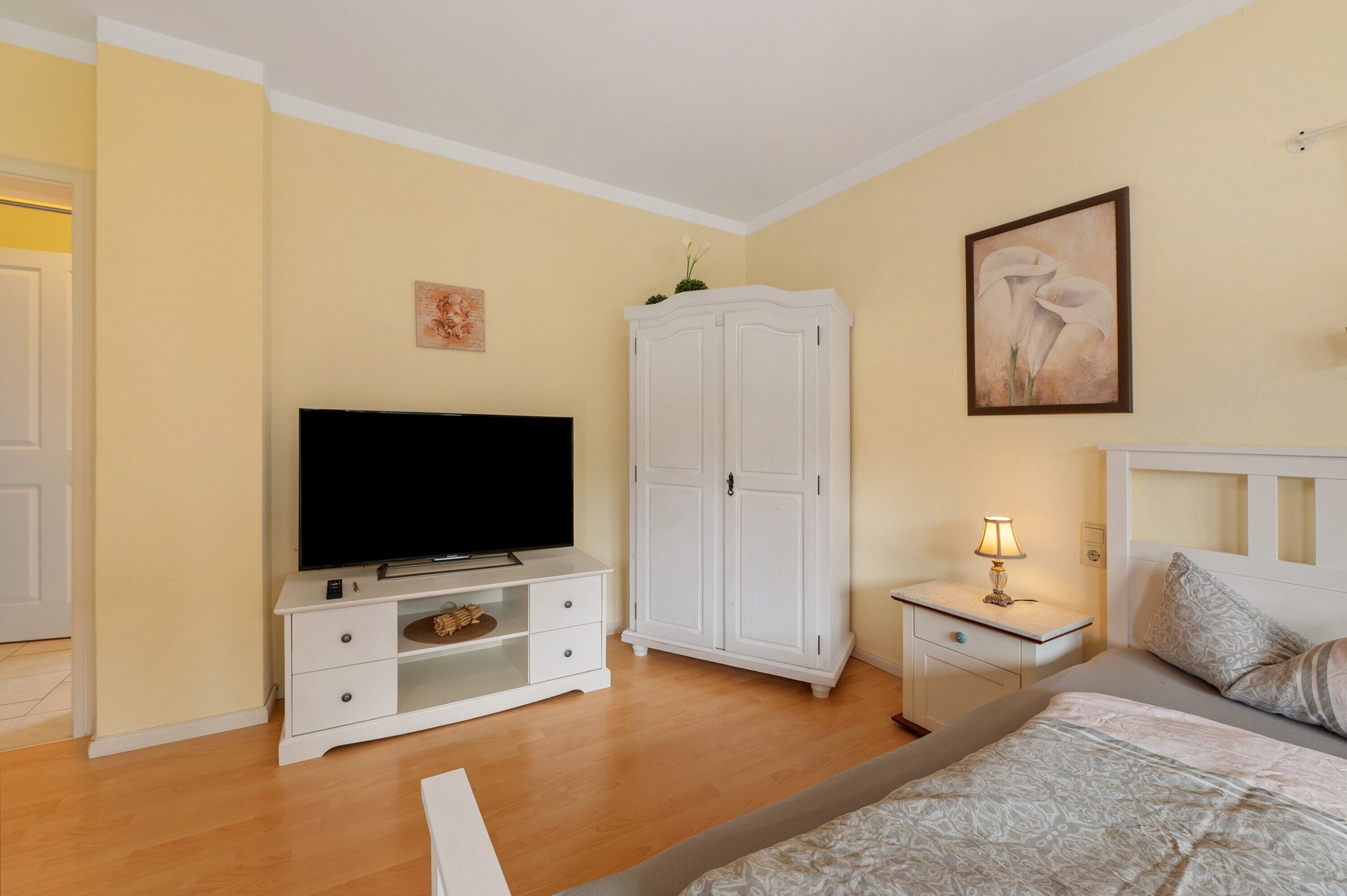 Une chambre à coucher avec un lit, une télévision, une armoire, une table de chevet et une lampe.