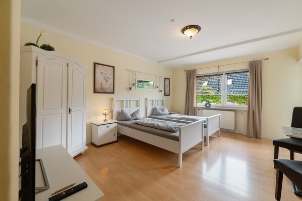 Ein Schlafzimmer mit Bett, Nachttischen, Schreibtisch, Stuhl, Kleiderschrank, einem Fenster mit Vorhängen und einer Deckenleuchte.
