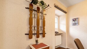 Ein Zimmer mit einer an der Wand befestigten Holzkonstruktion, einem kleinen Holzschrank mit Pflanze, einem Heizkörper und einem Stuhl.