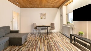 A room with a wooden ceiling, a gray sofa, a dining table with chairs, and a radiator.
