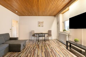 Une pièce avec un plafond en bois, un canapé gris, une table à manger avec des chaises et un radiateur.