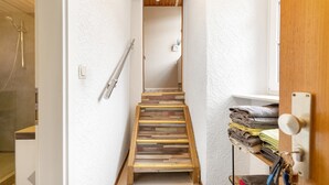 A narrow hallway with a wooden staircase, a towel rack, and a shower area.