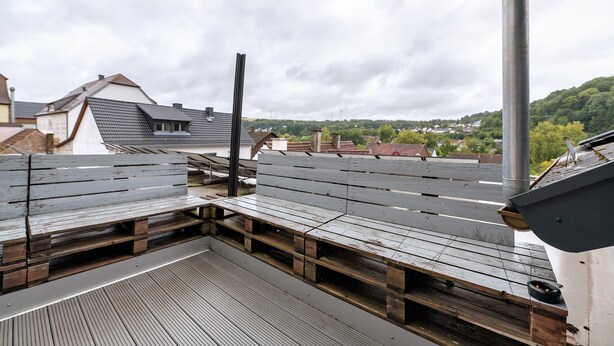 A rooftop terrace with wooden benches and a metal pole.