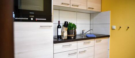 A modern kitchen with light wood cabinets, a black countertop, and a Siemens microwave.
