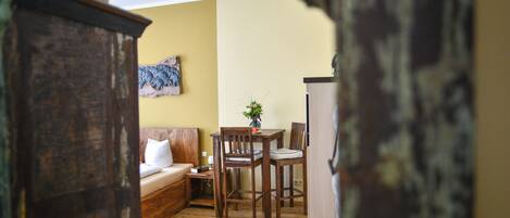 Una sala de estar acogedora con piso de madera, un sofá, una mesa de comedor con sillas, una mesita auxiliar y una planta en maceta.