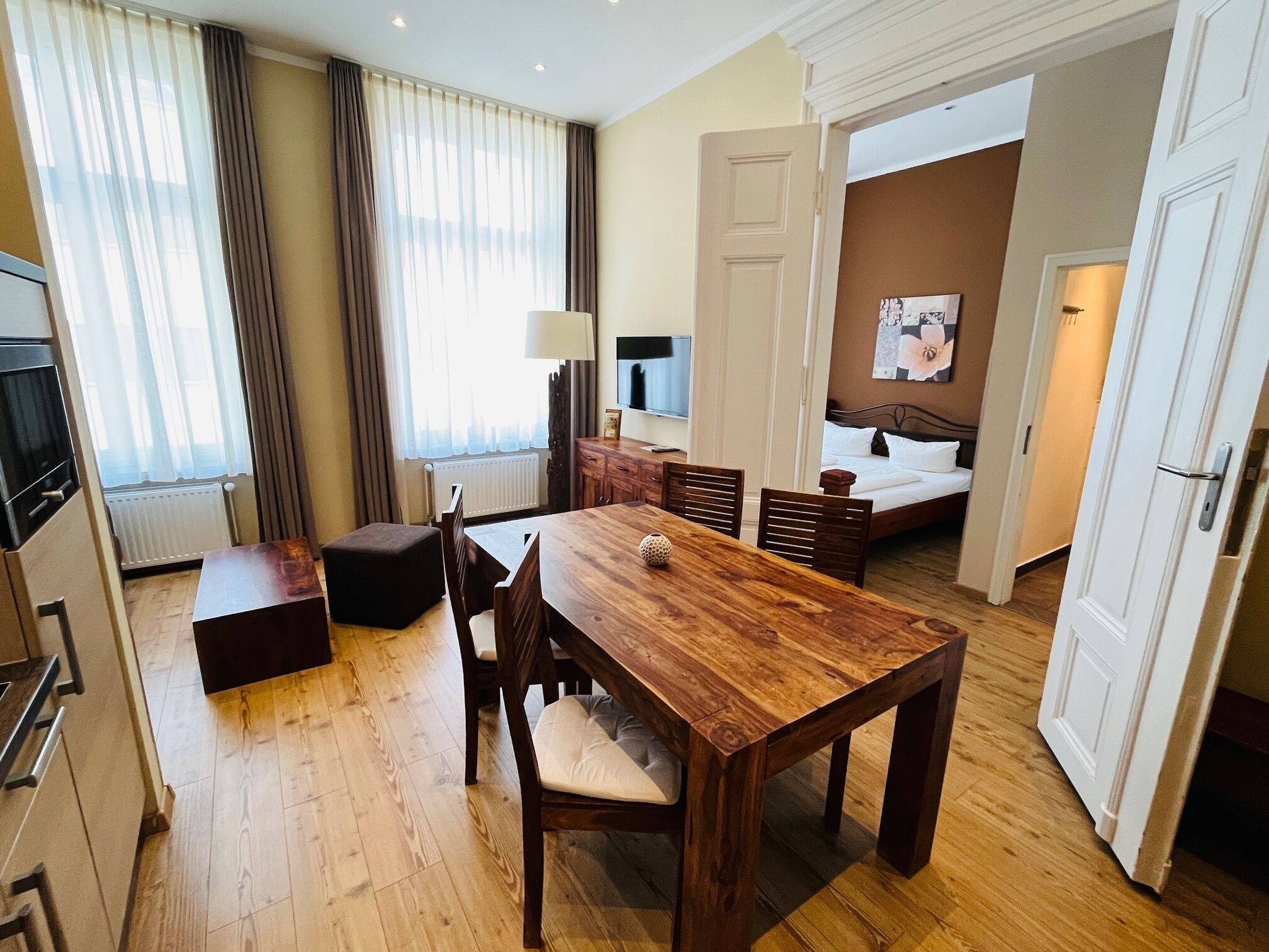 Habitación de hotel con una mesa de comedor de madera, sillas, un sofá, una cama, un televisor y un cuadro en la pared.