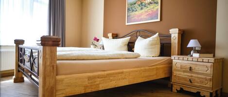 A bedroom with a wooden bed, a nightstand, a dresser, a painting on the wall, and a window with curtains.