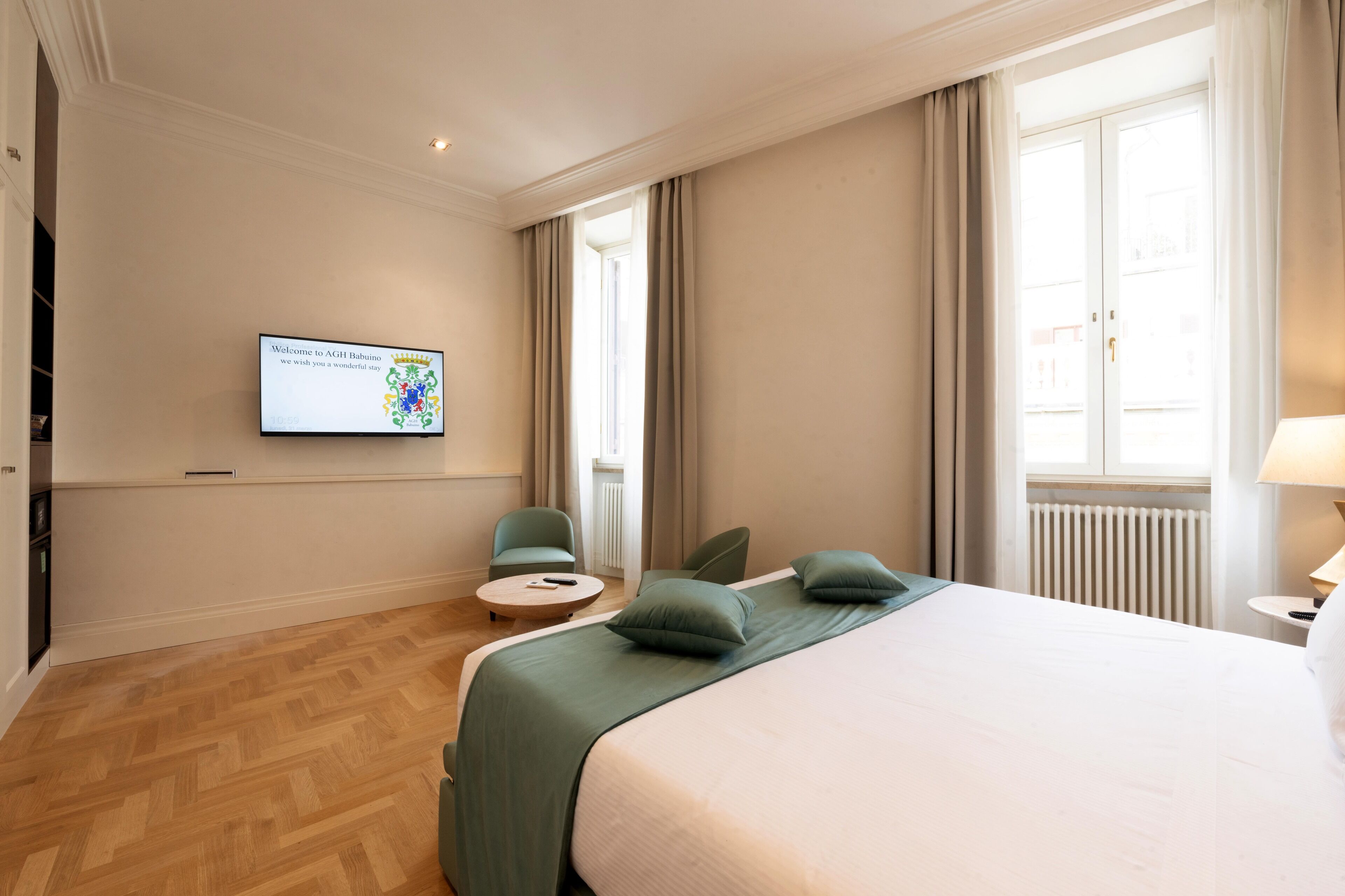 Habitación de hotel con cama, dos sillones, una mesita redonda, televisor en la pared y ventana con cortinas.