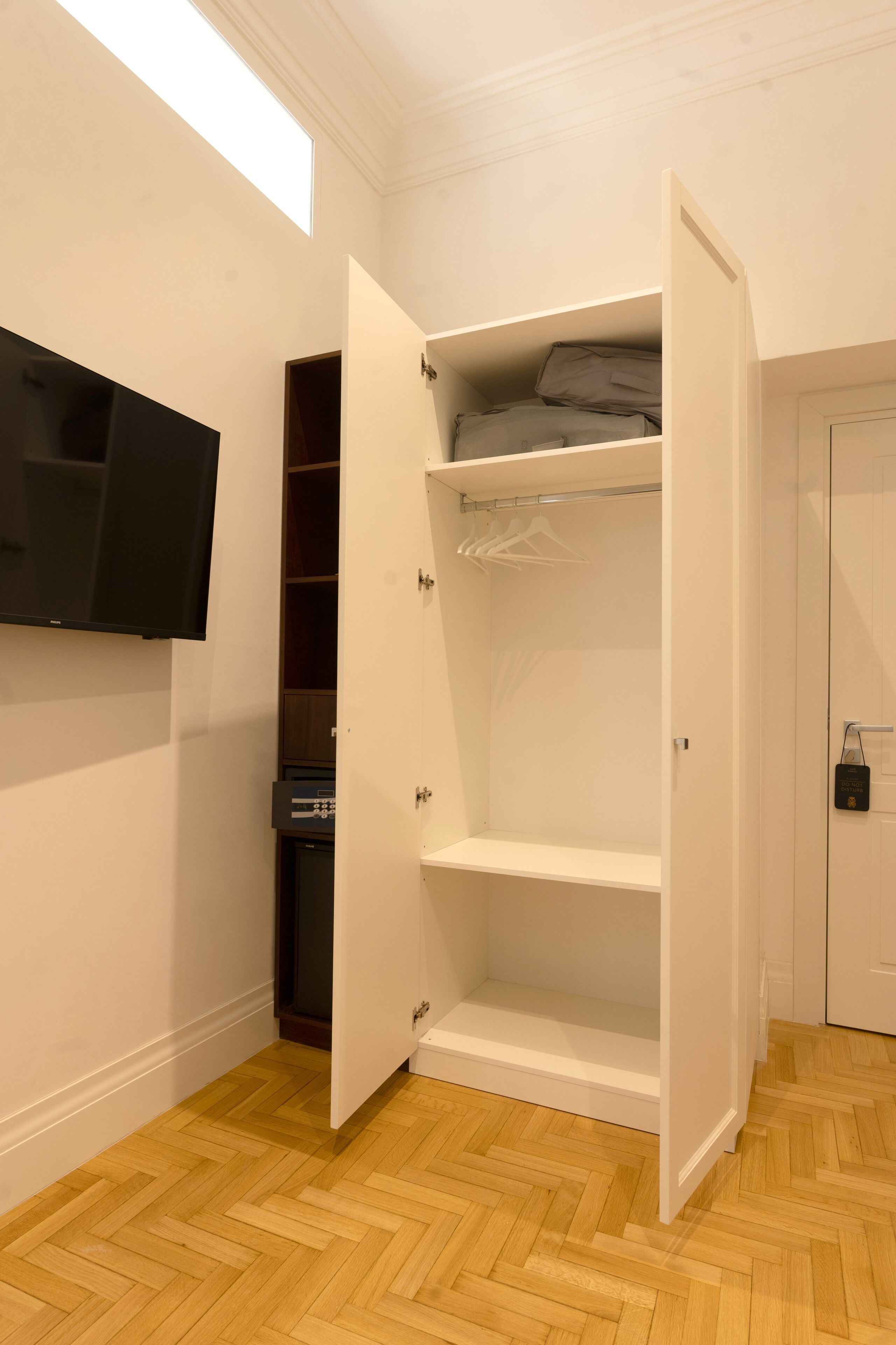 Una habitación con suelo de parqué, un armario blanco con espejo y un televisor de pantalla plana montado en la pared.