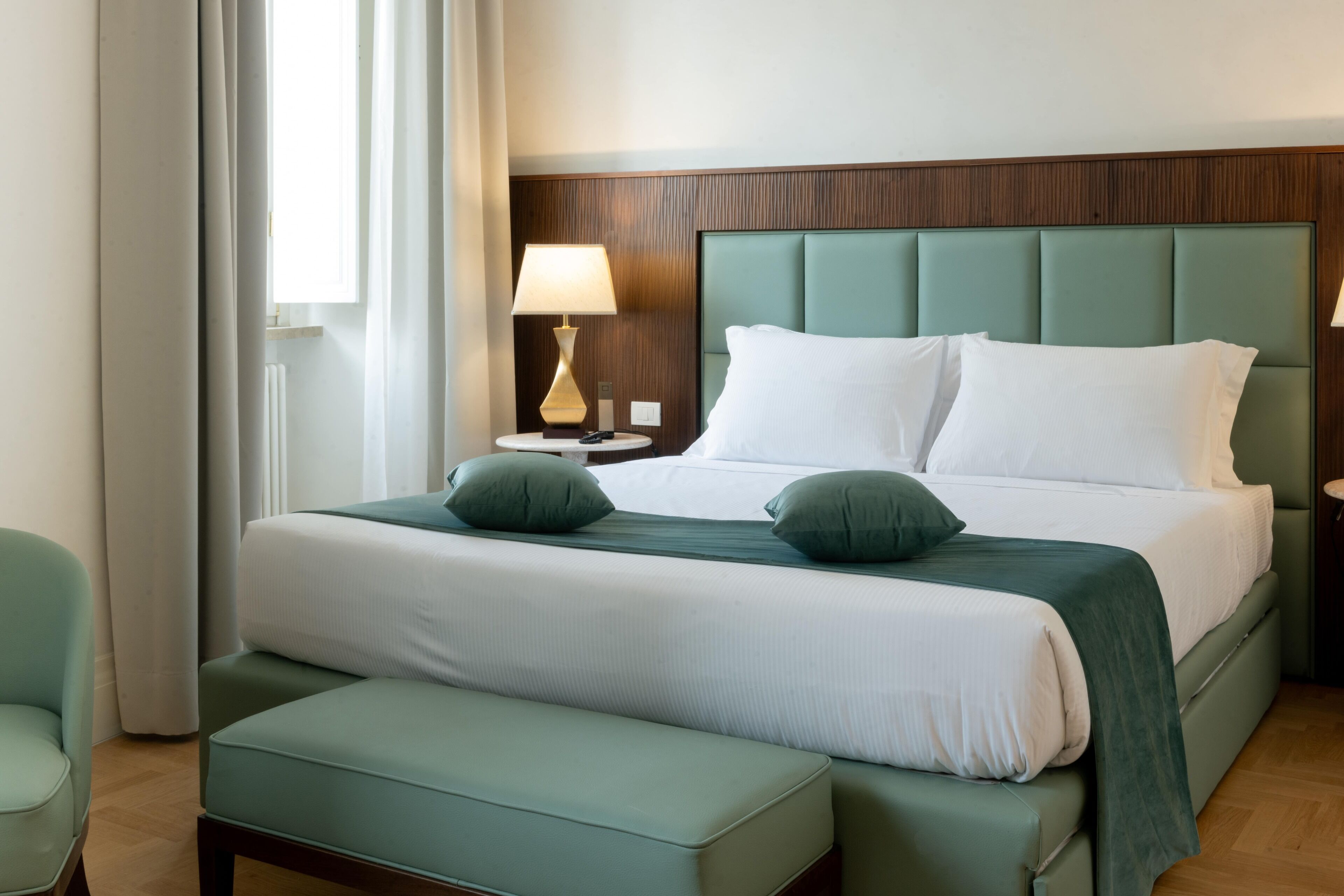 A hotel room with a large bed, two bedside tables, a bench, and a window with curtains.