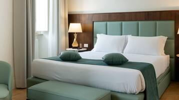 A hotel room with a large bed, two bedside tables, a bench, and a window with curtains.