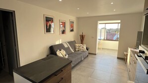 A modern living room with a sofa, a coffee table, and a kitchen area with a TV. - Quiet apartment with garden (Saint-Raphaël)