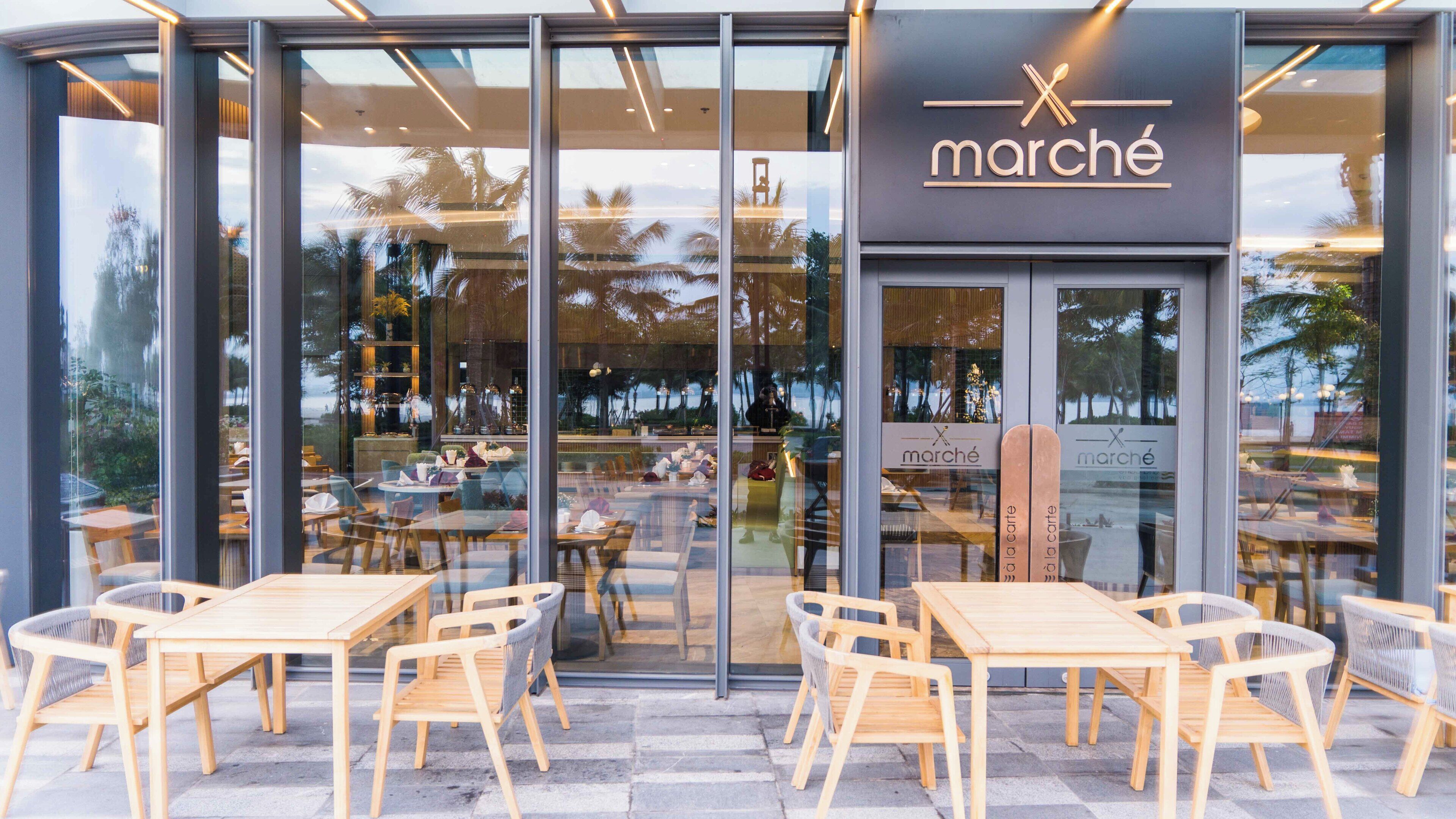 Ein modernes Café mit Glasfront, Holztischen und -stühlen und einem Schild mit der Aufschrift 'marché'.