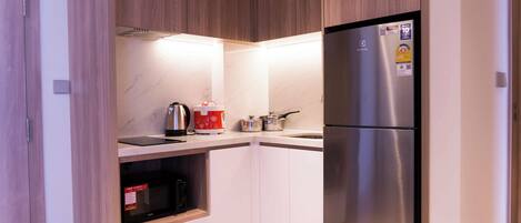 A compact kitchen with a stainless steel refrigerator, a microwave, a kettle, and a coffee maker.