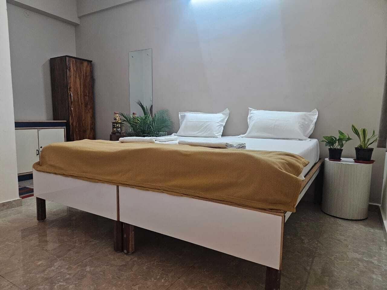 A bedroom with a bed, a wardrobe, a mirror, and two potted plants.