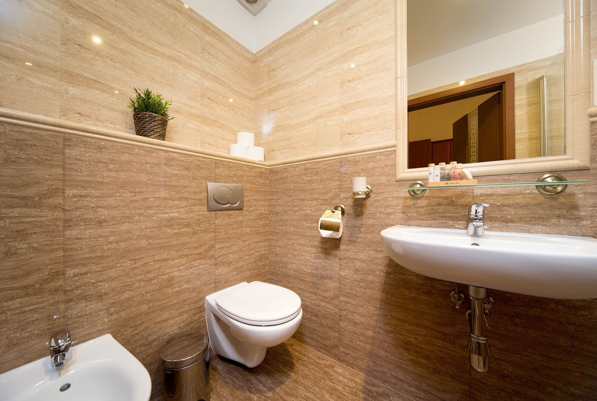 Un baño moderno con pared de mármol, inodoro blanco, lavamanos y bidé.