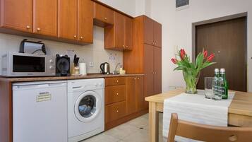 A compact kitchen with wooden cabinets, a microwave, a washing machine, a sink, and a table with a vase of red tulips and bottles.