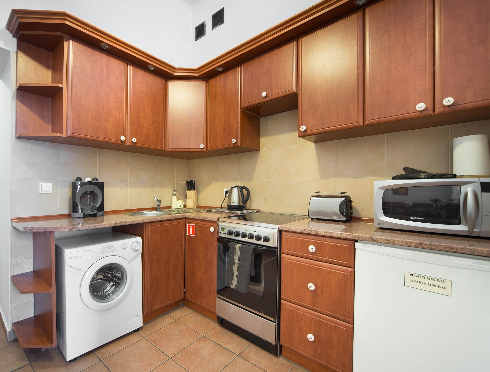 Una cocina compacta con armarios de madera, lavadora, estufa, microondas y tostadora.