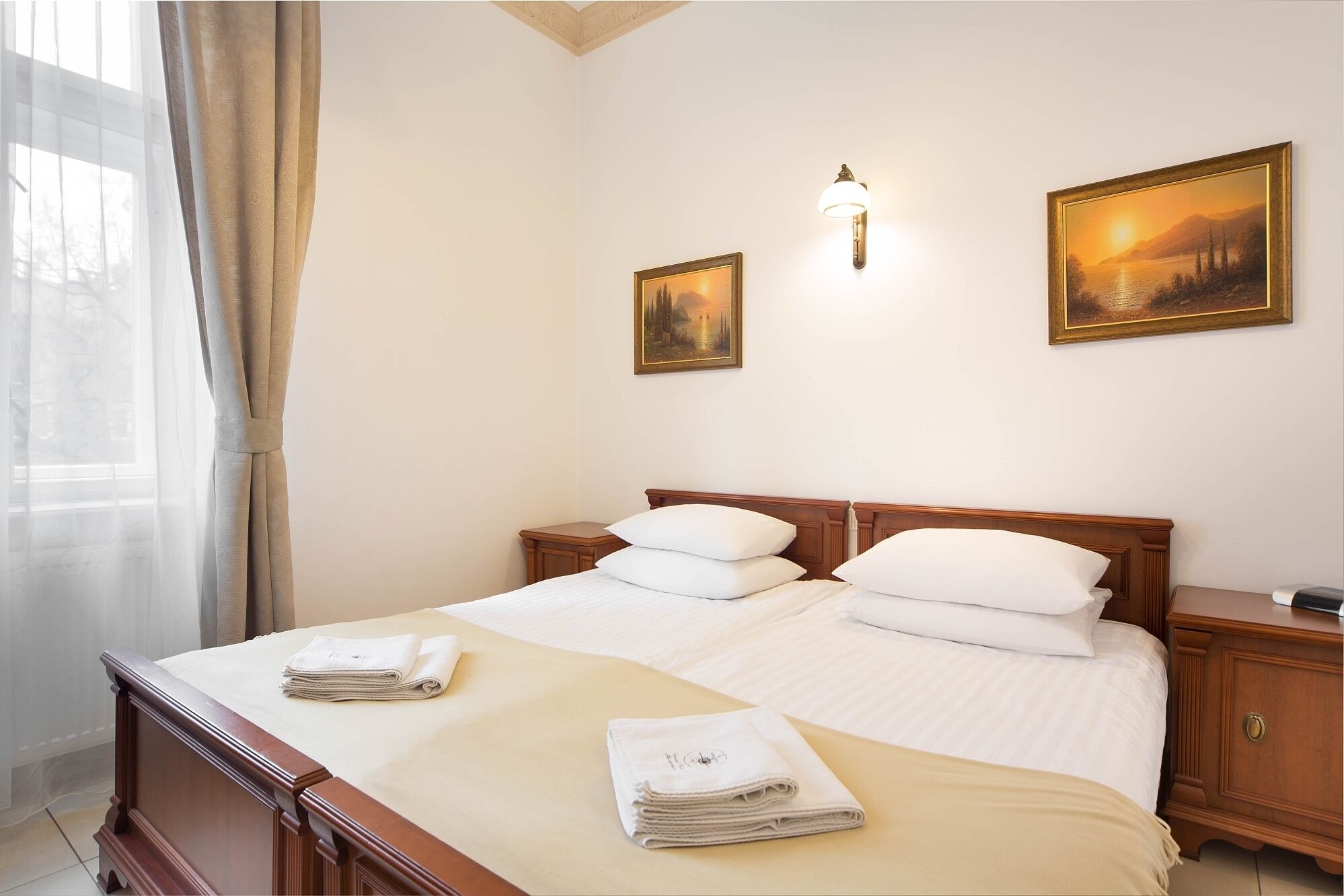 Habitació d'hotel amb un llit de matrimoni, dues tauletes de nit, una làmpada penjada a la paret i dues imatges amb marc.