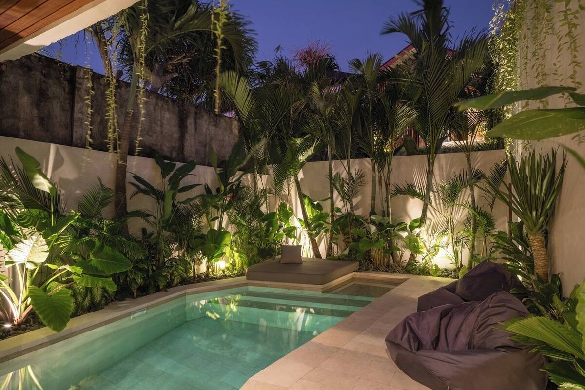 A pool area with a built-in seating area and lush tropical plants.