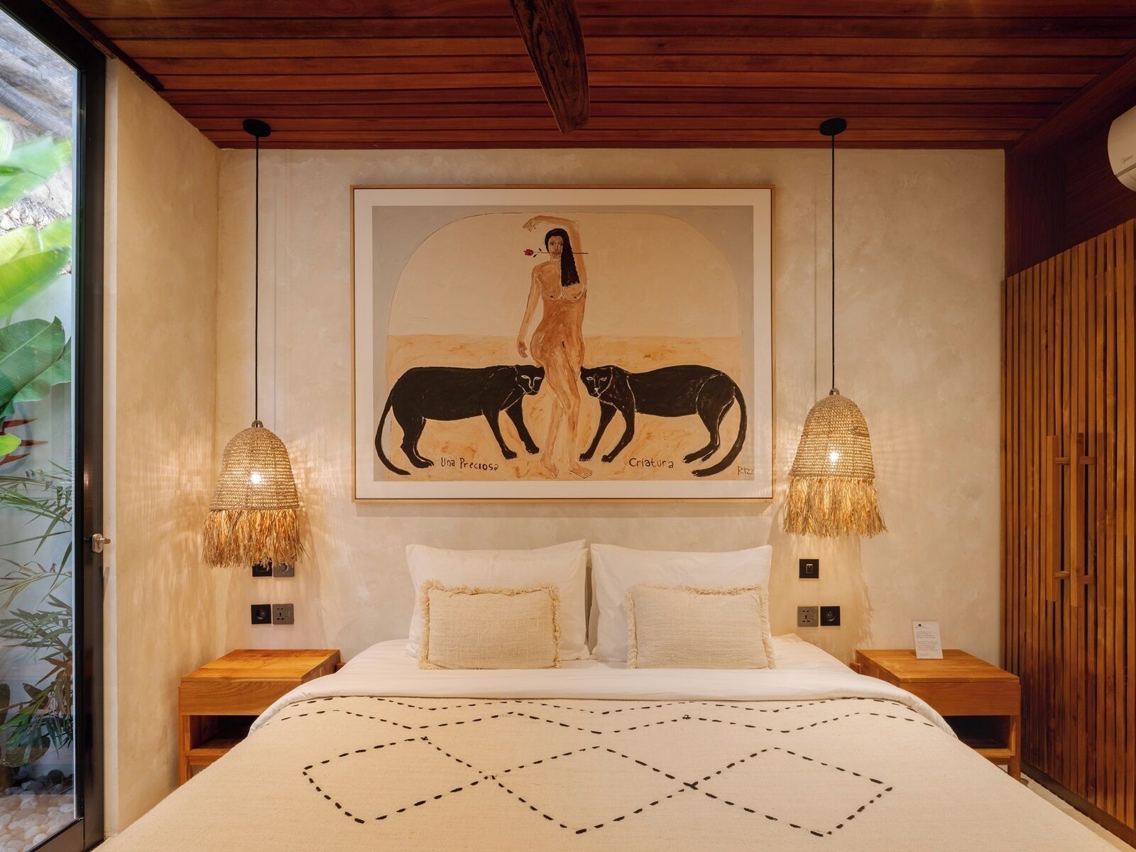 A bedroom with a bed, two bedside tables, a framed artwork above the bed, and a wooden ceiling.
