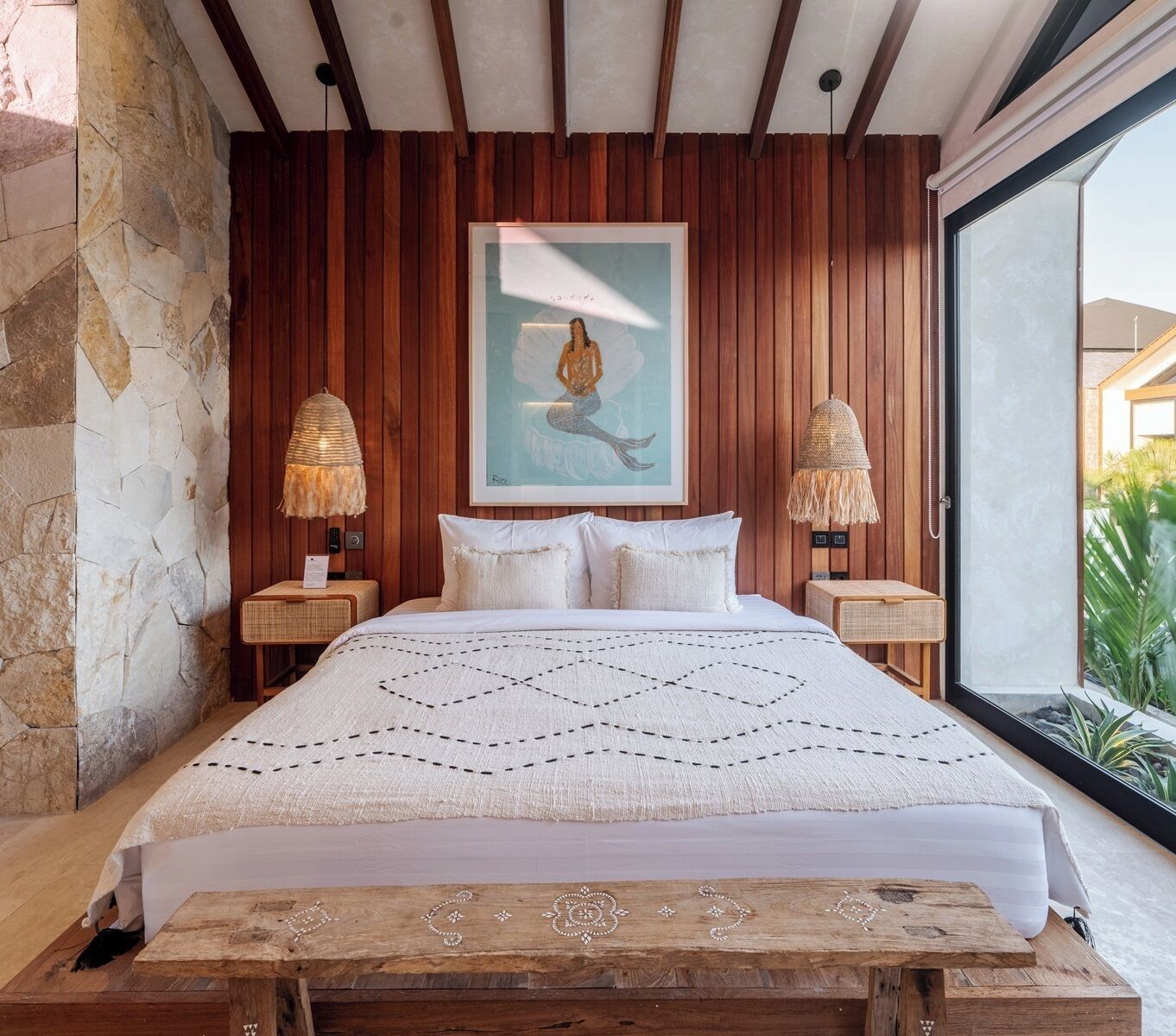 Ein Schlafzimmer mit Steinwand, Holzvertäfelung, einem großen Bett mit weißer Bettwäsche, zwei Nachttischlampen und einem gerahmten Kunstwerk an der Wand.
