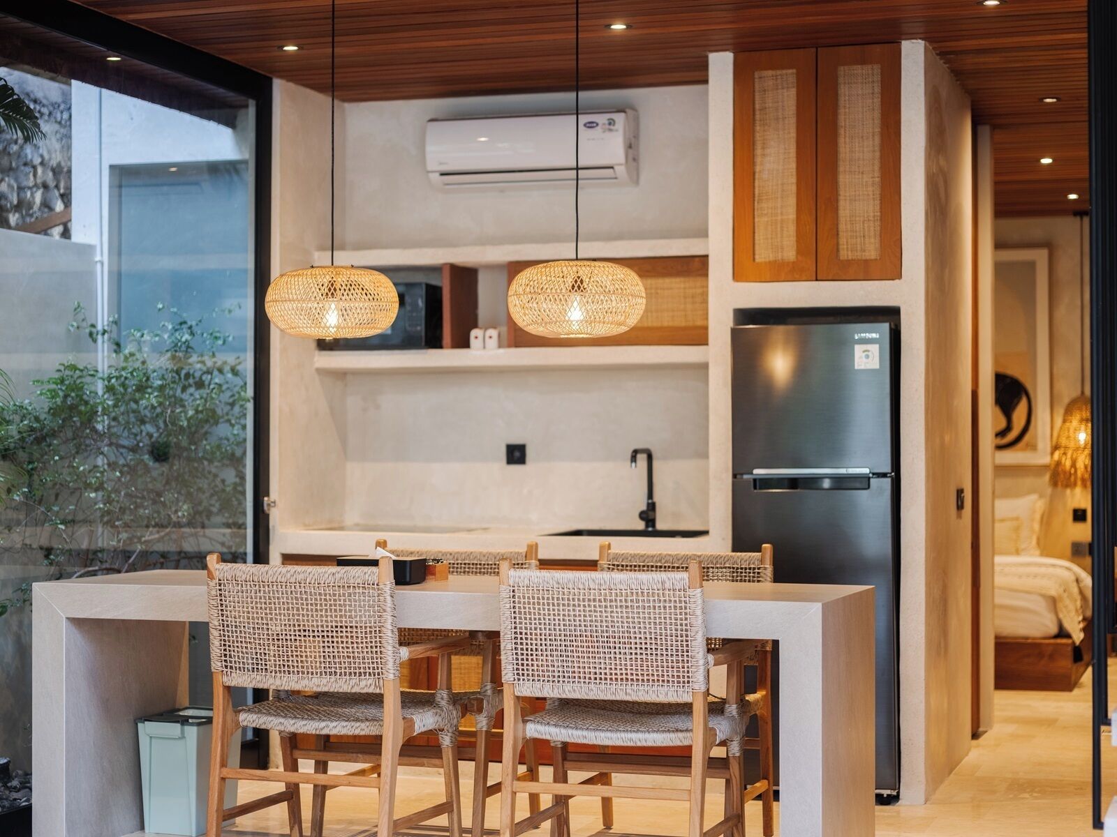 A modern kitchen with a built-in island, wicker chairs, and a stainless steel refrigerator.