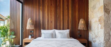 A bedroom with a wooden slatted ceiling, a stone accent wall, a large bed with a white bedspread, and two bedside lamps.