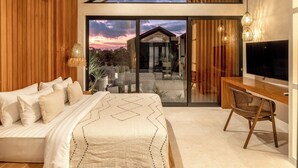 Un dormitorio moderno con una cama grande, un escritorio y un televisor. Cuenta con paneles de madera, un ventanal y vistas a una casa.