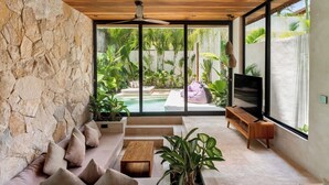 Una sala de estar moderna con pared de piedra, techo de madera, televisor y vista a un jardín.