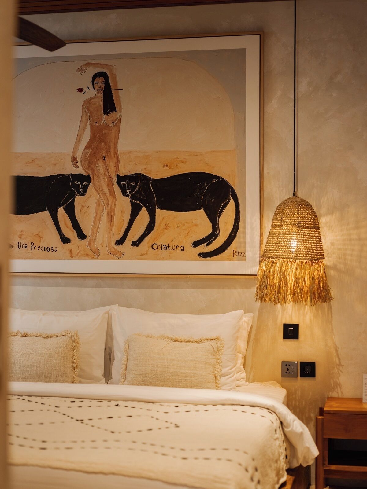 Een slaapkamer met een bed, kussens, een aan de muur hangend kunstwerk en een hanglamp.