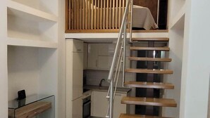 A modern interior with a wooden staircase, a kitchen area, and a mezzanine with a slatted wooden wall. - Corfu Luxury Loft2 by Corfuescapes (Corfu)